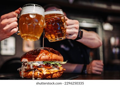 man and woman hands clinking with glasses of light beer at the pub or bar and very big burger - Powered by Shutterstock