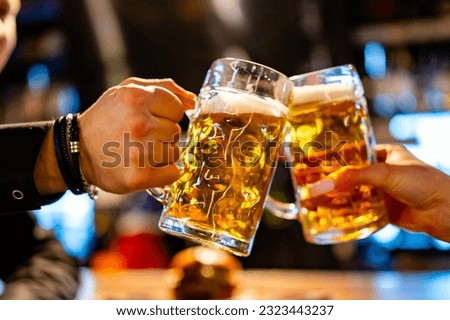 man and woman hands clinking with glasses of light beer at the pub or bar