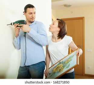 Man And Woman  Hanging   Picture On Wall At Home