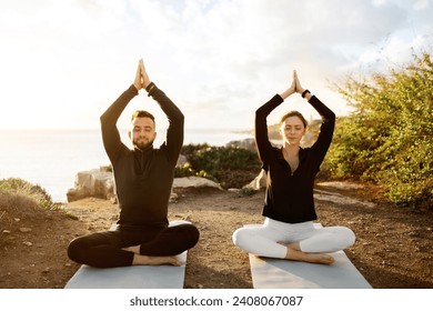 Man and woman in harmonious yoga poses meditating during sunset on tranquil coastal path, reflecting balanced and mindful lifestyle - Powered by Shutterstock