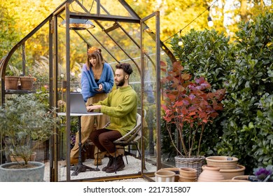 Man and woman have a conversation while work on laptop by the round table in glass house with plants and flowers at backyard. Work from home at cozy atmosphere on nature - Powered by Shutterstock