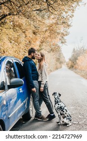 Man With Woman Have Fun With Their Dog Outdoors In Forest Near Modern Black Car.