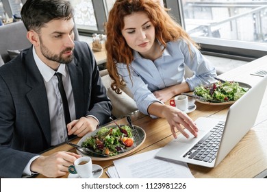 Man And Woman Having Business Lunch At Restaurant Sitting At Table Eating Salad Drinking Hot Coffee Browsing Laptop Concentrated Serious