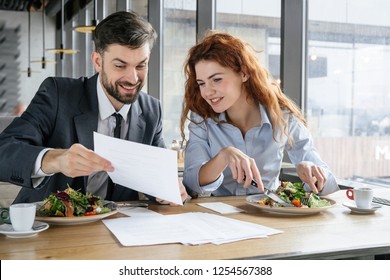 Man and woman having business lunch at restaurant sitting at table eating fresh salad guy showing his collegue document conditions smiling happy - Powered by Shutterstock