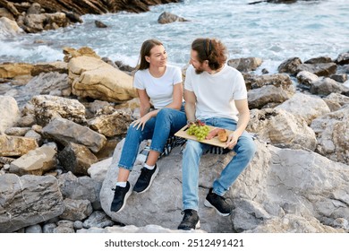 A man and woman having a picnic on rocky beach, sharing a moment with the ocean in background. - Powered by Shutterstock