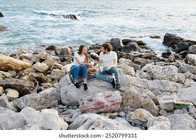 A man and woman having a picnic on rocky beach with gentle waves in the background. - Powered by Shutterstock