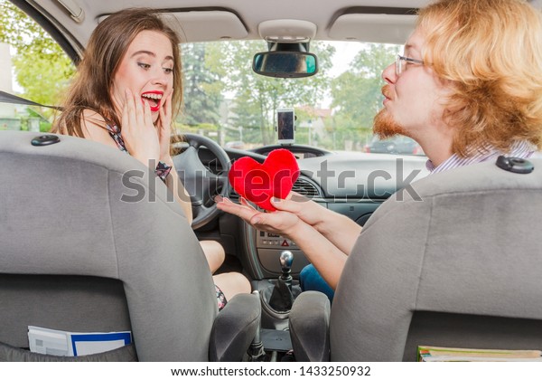 Man and woman having romance in car. Female\
received heart shaped pillow gift from her boyfriend. Relationship,\
valentines day concept.