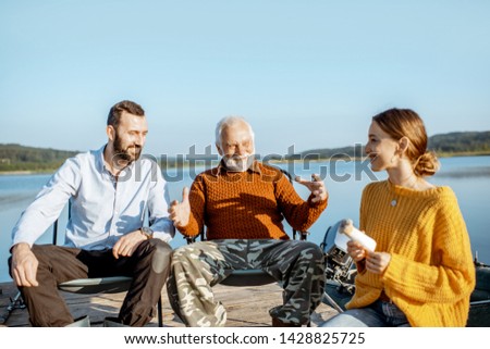 Man and woman having warm conversation with senior grandfather during the picnic near the lake in the morning