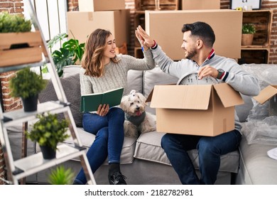 Man And Woman High Five Sitting On Sofa With Dog At New Home