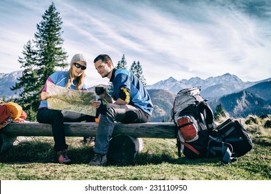 Man and woman hikers hiking in mountains. Young couple camping, looking at map and planning trip or get lost. Getting rest and drinking coffee or tea, navigation and looking for direction - Powered by Shutterstock