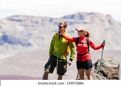 Man And Woman Hikers Trekking In Summer Mountains. Young Couple On Rocky Mountain Range Looking At Beautiful View. Hiking On Volcano Mountain, Tenerife Canary Islands