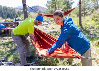 Man and woman in hiking equipment setting up a hammock between trees at the top of the mountain.