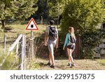 Man and woman hiking in Infected ticks forest with warning sign. Risk of tick-borne and lyme disease.