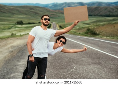 A man and a woman are hitchhiking. Wanderlust, autostop journey concept. Young people traveling hitchhiking. Tourists catches car on road. Hitchhiking couple on the road. Copy space