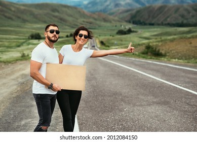 A man and a woman are hitchhiking. Wanderlust, autostop journey concept. Young people traveling hitchhiking. Hitchhiking couple on the road. Hitchhiking trip. Car travel. Two by the road. Copy space