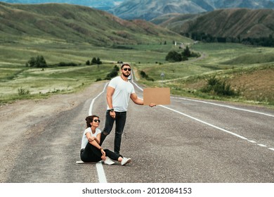 A man and a woman are hitchhiking. Wanderlust, autostop journey concept. Young people traveling hitchhiking. Hitchhiking couple on the road. Hitchhiking trip. Car travel. Two by the road. Copy space