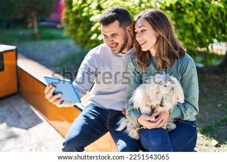 Man and woman holding dog having video call by touchpad at park