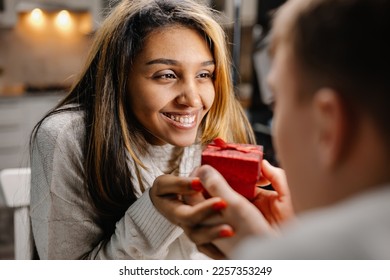 A man and a woman are holding a gift. A couple in love is sitting at a table and looking into each other's eyes holding hands. Coffee mugs and heart-shaped cakes. A lovers celebrates Valentine's Day