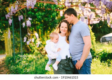 Man and woman holding their baby girl under a wysteria tree in the park
