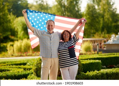 Man and woman holding the usa flag. Patriotic married mature couple. Green summer park background. - Powered by Shutterstock