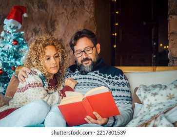 Man And Woman At Home Enjoying Holiday Season And Christmas Time Having Relax Leisure Indoor Activity Together. People In Relationship. Mature Male Reading A Book. Female Hugging Husband And Smile