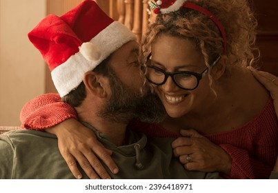 Man and woman at home wearing santa claus hat kissing with love and romance.. Happy couple in relationship enjoy christmas holiday season. Woman hugging man and apartment in background. New year - Shutterstock ID 2396418971