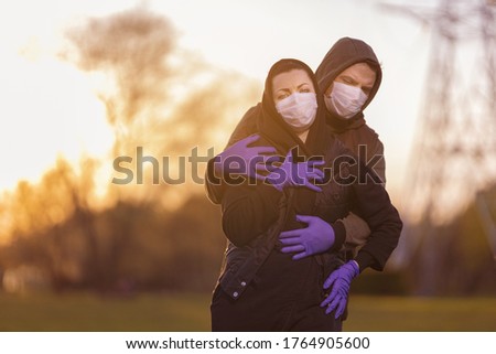 A man and a woman in hoods, in protective masks and purple gloves posing in the setting sun in the city.