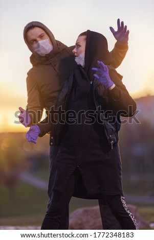 A man and a woman in hoods, in protective masks and purple gloves posing in the setting sun in the city.