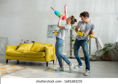 Man And Woman With Household Singing While Doing Spring Cleaning In Living Room