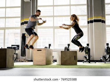 Man and woman jumping on boxes in gym