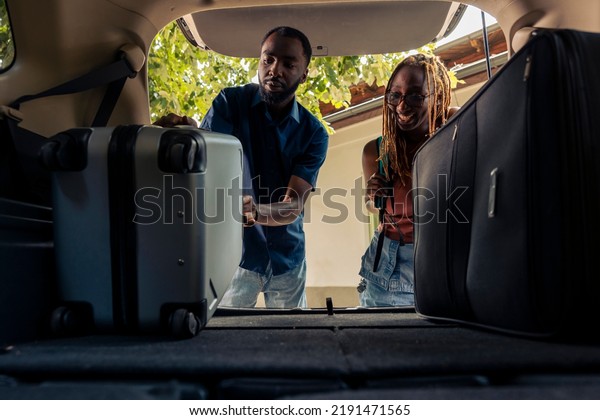 Man and\
woman loading baggage in vehicle trunk, leaving on summer holiday\
together. Couple preparing car with travel bags and luggage to go\
on vacation trip and drive to\
destination.