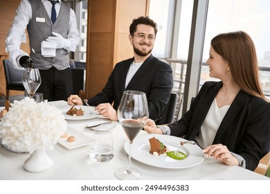 Man and woman looking each other in restaurant while waiter pouring wine - Powered by Shutterstock