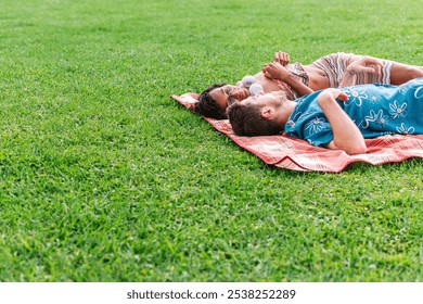 A man and a woman are lying on a blanket in a grassy field in a park. The man is wearing a blue shirt with flowers. The woman is lying on her back with her arms crossed. The scene is peaceful. - Powered by Shutterstock