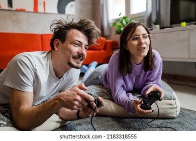 Man And Woman Lying On The Floor At Home Playing Video Game Console