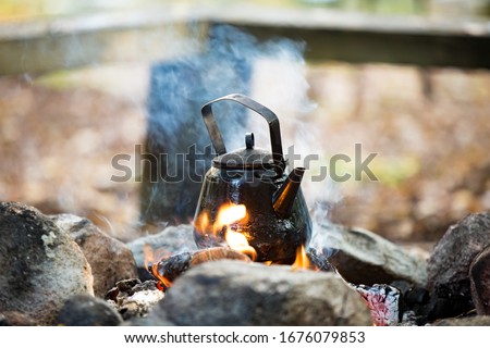 Man and woman making coffee in big kettle on campfire in forest on shore of lake, making a fire, grilling. Happy couple exploring Finland. Scandinavian landscape. 