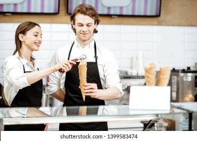 Man And Woman Making Ice Cream In Waffle Cones For Selling, Standing Together At The Counter Of The Modern Shop