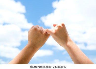 Man and woman making a pinkie promise with blue sky background