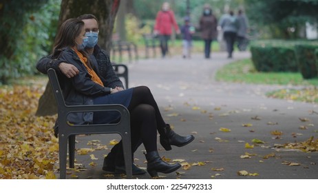 Man and woman with mask sit on bench in park, autumn foliage, different freedom - Shutterstock ID 2254792313