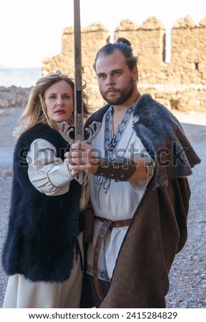 A man and woman in medieval costume hold a decorative sword together, evoking historical drama and romance.