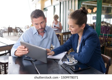 man and woman meeting in cafe looking at tablet pc