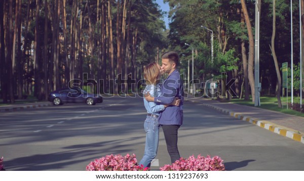 Man and woman meeting in the park. Caucasian happy\
couple on a date kissing and smiling. Handsome guy and attractive\
girl looking with smile. People wearing in casual dress denim shirt\
and blue
