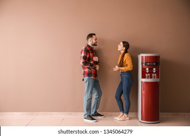 Man And Woman Near Water Cooler Against Color Wall