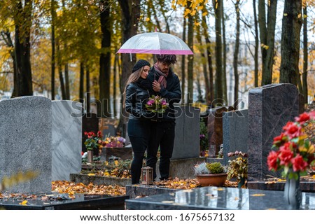 Man and woman on a cemetery with flowers and fallen autumn leaves
