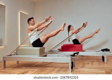 A man and a woman in a pair do pilates exercises on reformers, diversity man and woman, paired exercises on a reformer to restore the musculoskeletal system, pilate, reformer - Powered by Shutterstock