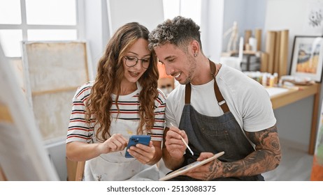 A man and woman, partners in a bright art studio, collaborate while browsing a smartphone and holding a paintbrush. - Powered by Shutterstock