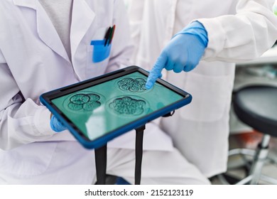 Man and woman partners wearing scientist uniform pointing with finger to embryo image touchpad at laboratory