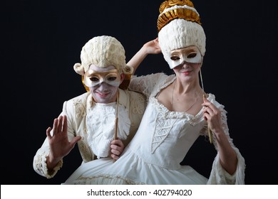 A Man And A Woman In Period Costume And Wigs And Holding A Theatrical Mask