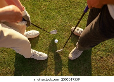 man and woman playing golf on the course at sunset, close-up of golf ball and clubs and people's feet on green grass, couple competing in the game and hitting the ball into the hole - Powered by Shutterstock