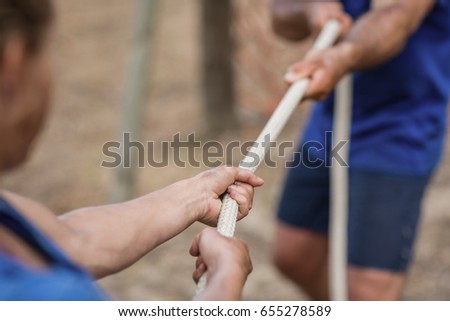 Man and woman playing tug of war during obstacle course in boot camp