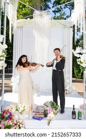 Man and woman playing violins under the wedding arch.